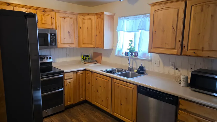 Kitchen with stainless steel appliances, light countertops, dark wood-style flooring, and light wood finish cabinets