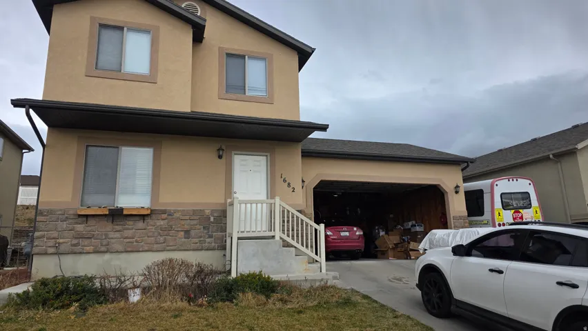 View of front of property featuring stucco siding, stone siding, an attached garage, and driveway
