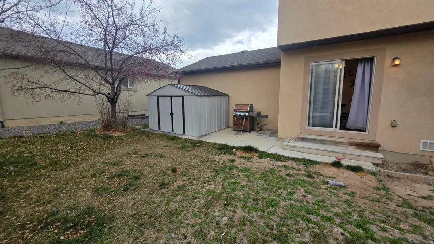 View of home's exterior featuring stucco siding, a storage shed, a lawn, and entry steps