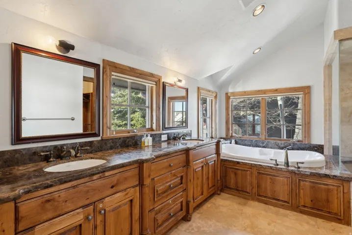 Full bath with vaulted ceiling, double vanity, recessed lighting, and a garden tub
