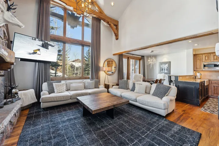 Living room with suspended lighting, dark wood-style flooring, and a high ceiling