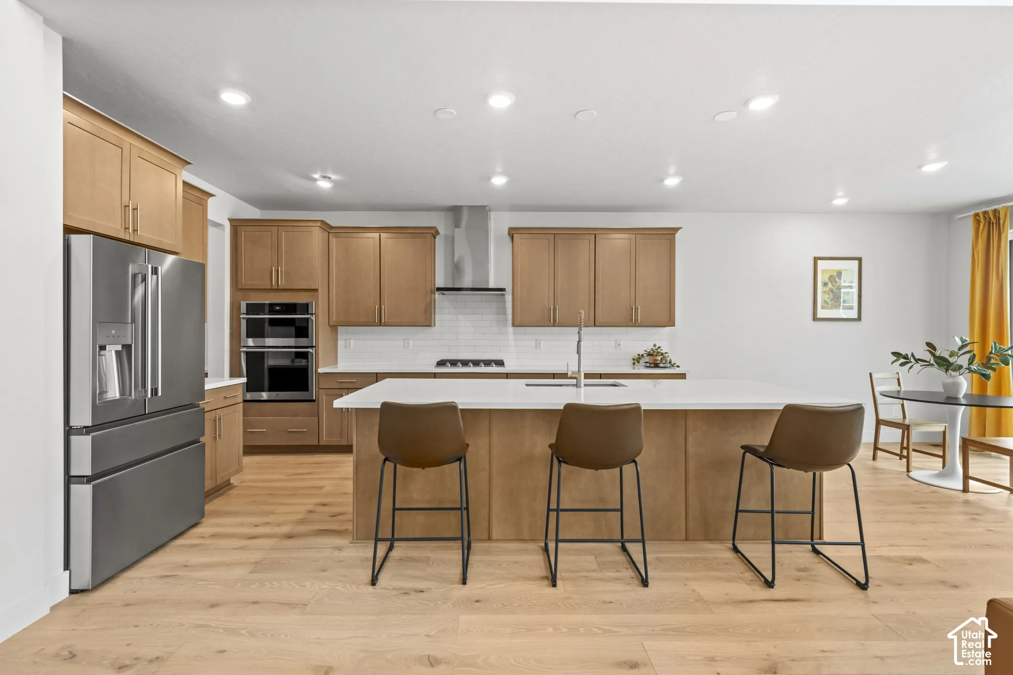 Kitchen featuring stainless steel appliances, light wood LVP flooring, a kitchen bar, recessed lighting, and a center island with sink