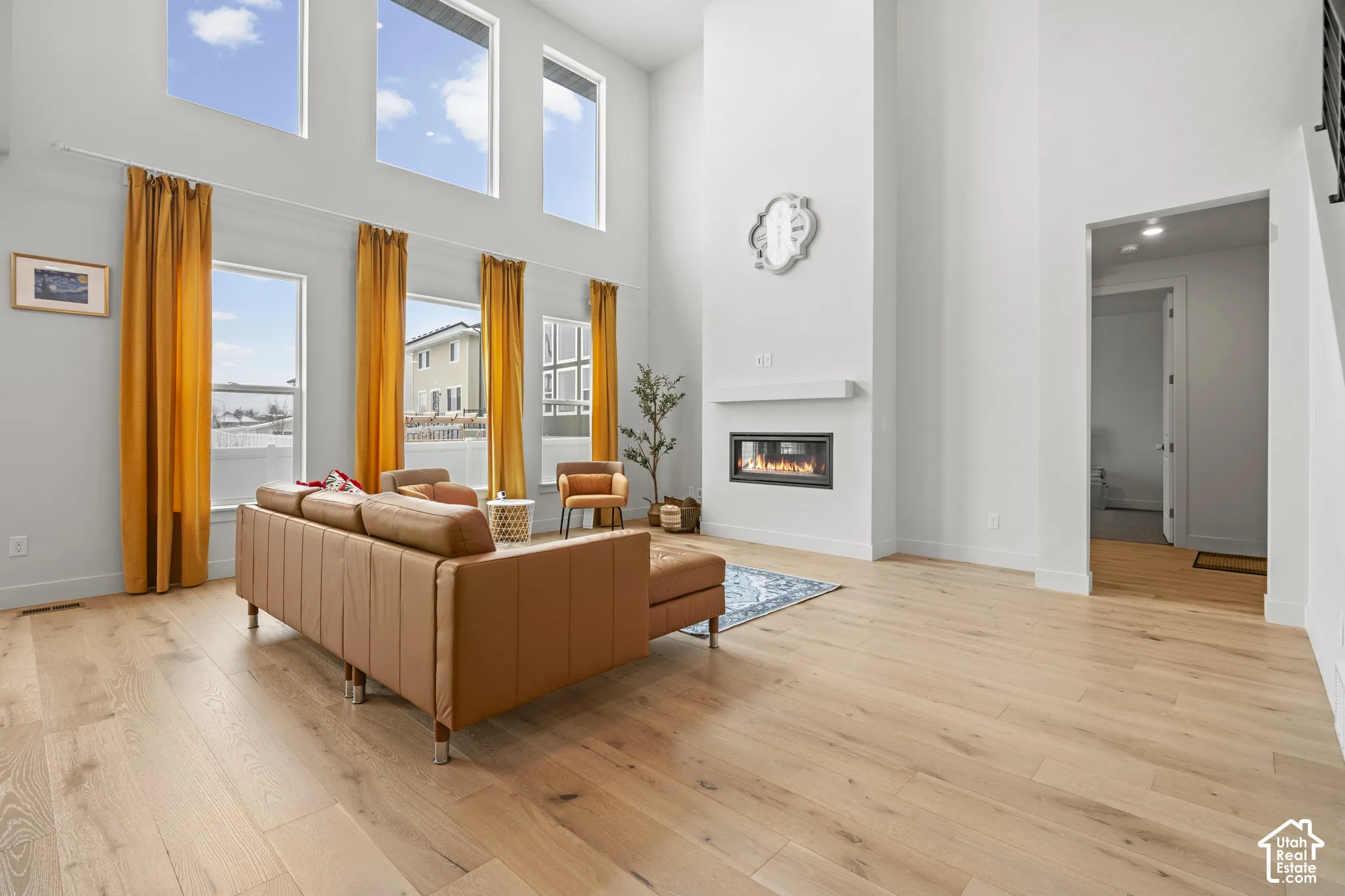Living room featuring a high ceiling, light LVP wood flooring, a glass covered fireplace, and plenty of natural light
