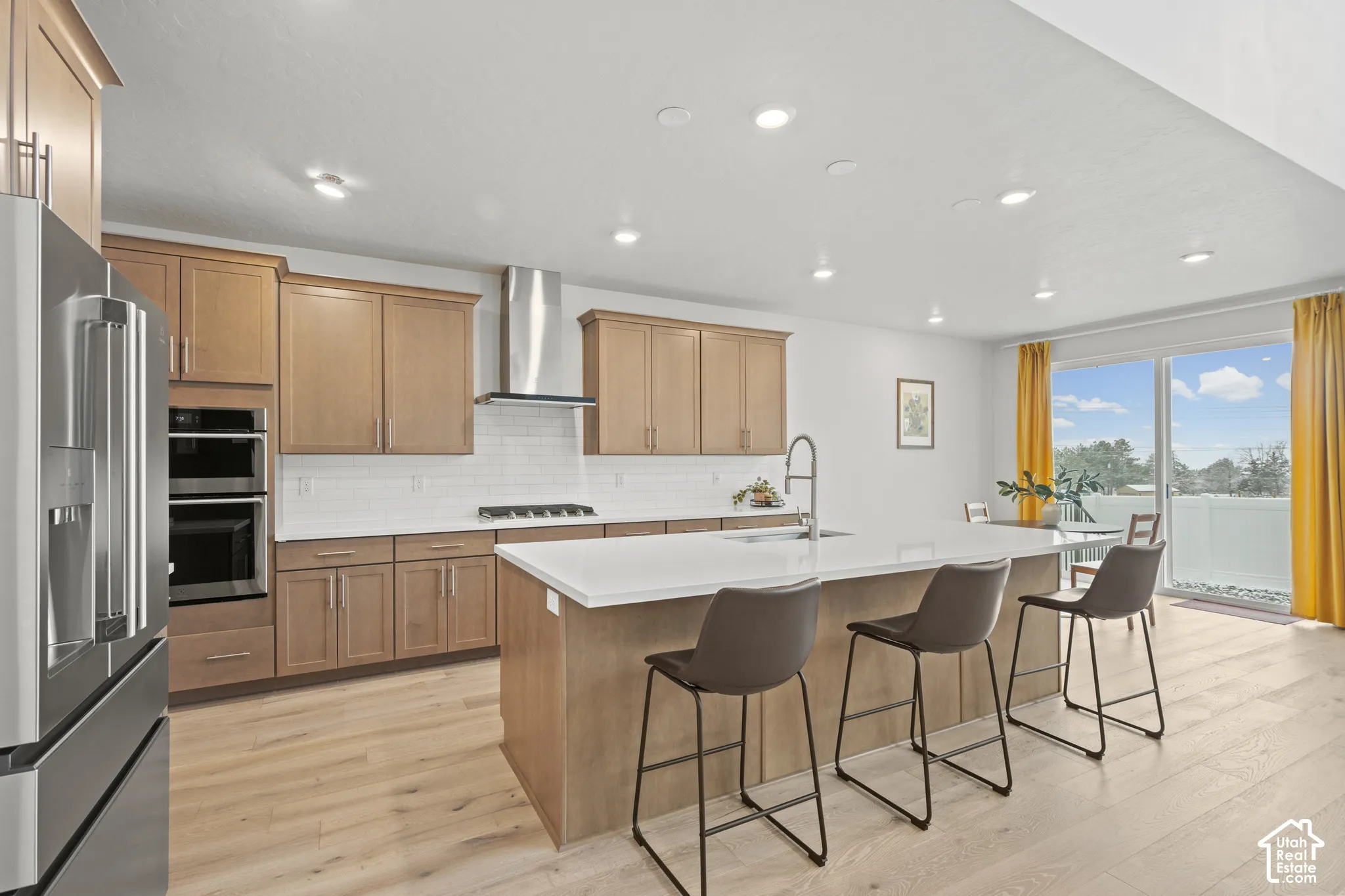 Kitchen with stainless steel appliances, a kitchen island with sink, a kitchen breakfast bar, light wood LVP floors, and recessed lighting