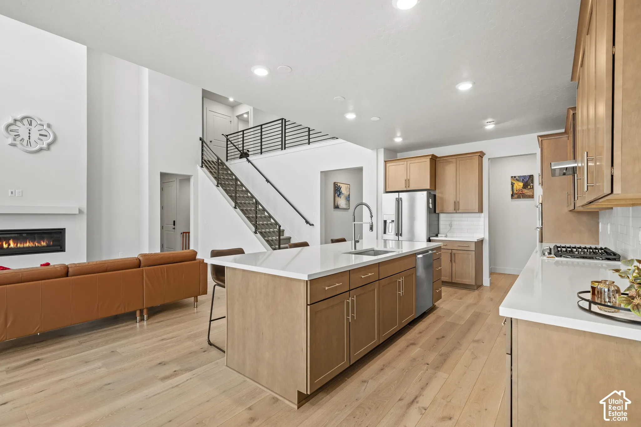 Kitchen featuring a breakfast bar area, light wood LVP flooring, open floor plan, stainless steel appliances, and a glass covered fireplace