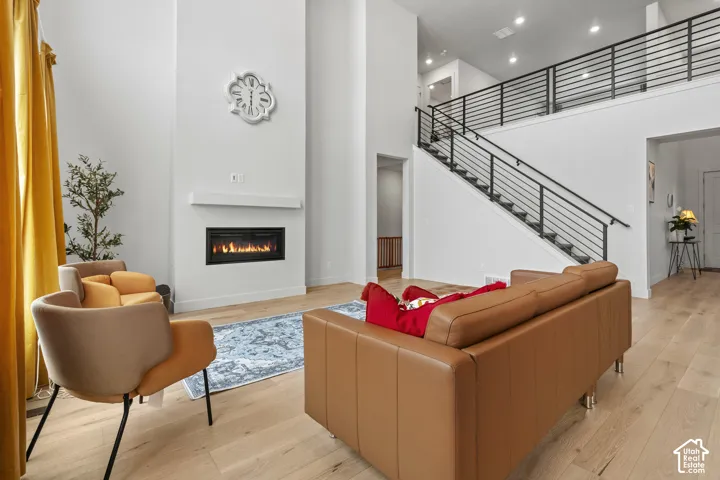 Living room featuring a high ceiling, light LVP wood flooring, a glass covered fireplace, and plenty of natural light