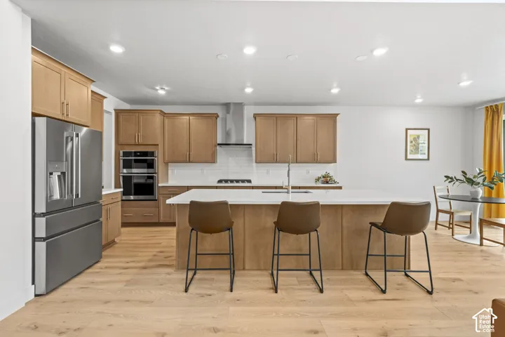 Kitchen featuring stainless steel appliances, light wood LVP flooring, a kitchen bar, recessed lighting, and a center island with sink