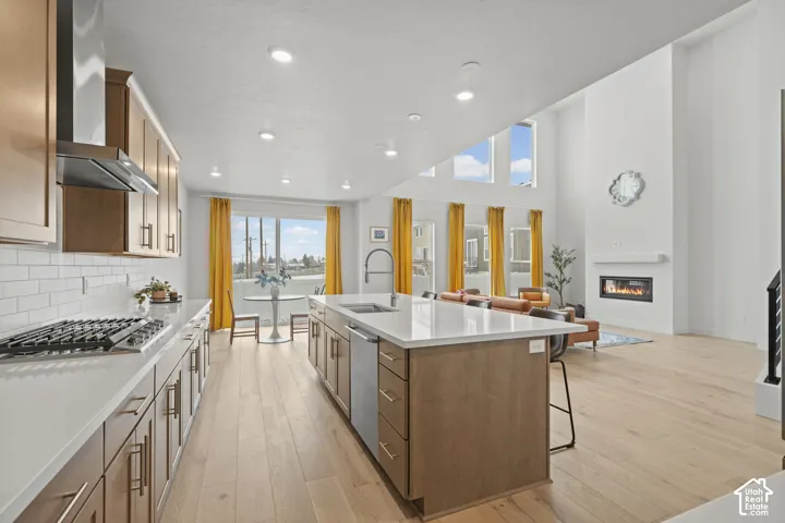 Kitchen with stainless steel appliances, a kitchen island with sink, a kitchen breakfast bar, light wood LVP floors, recessed lighting a high ceiling