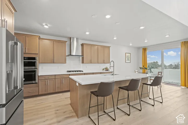 Kitchen with stainless steel appliances, a kitchen island with sink, a kitchen breakfast bar, light wood LVP floors, and recessed lighting