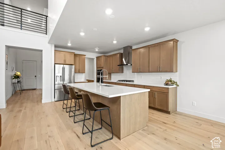 Kitchen with a breakfast bar, stainless steel appliances, an island with sink, light wood LVP finished floors, and recessed lighting