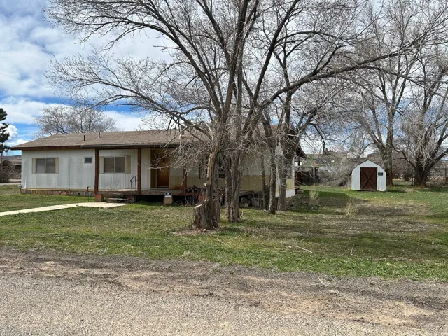 View of front of house featuring a storage shed, a front yard, a shingled roof, and covered porch