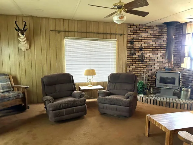 Sitting room featuring a wood stove, carpet floors, and ceiling fan