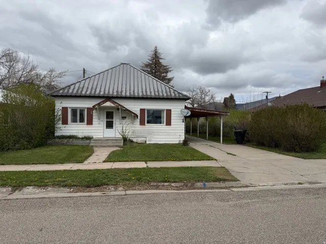 View of front of house featuring an attached carport, a metal roof, driveway, and a front lawn