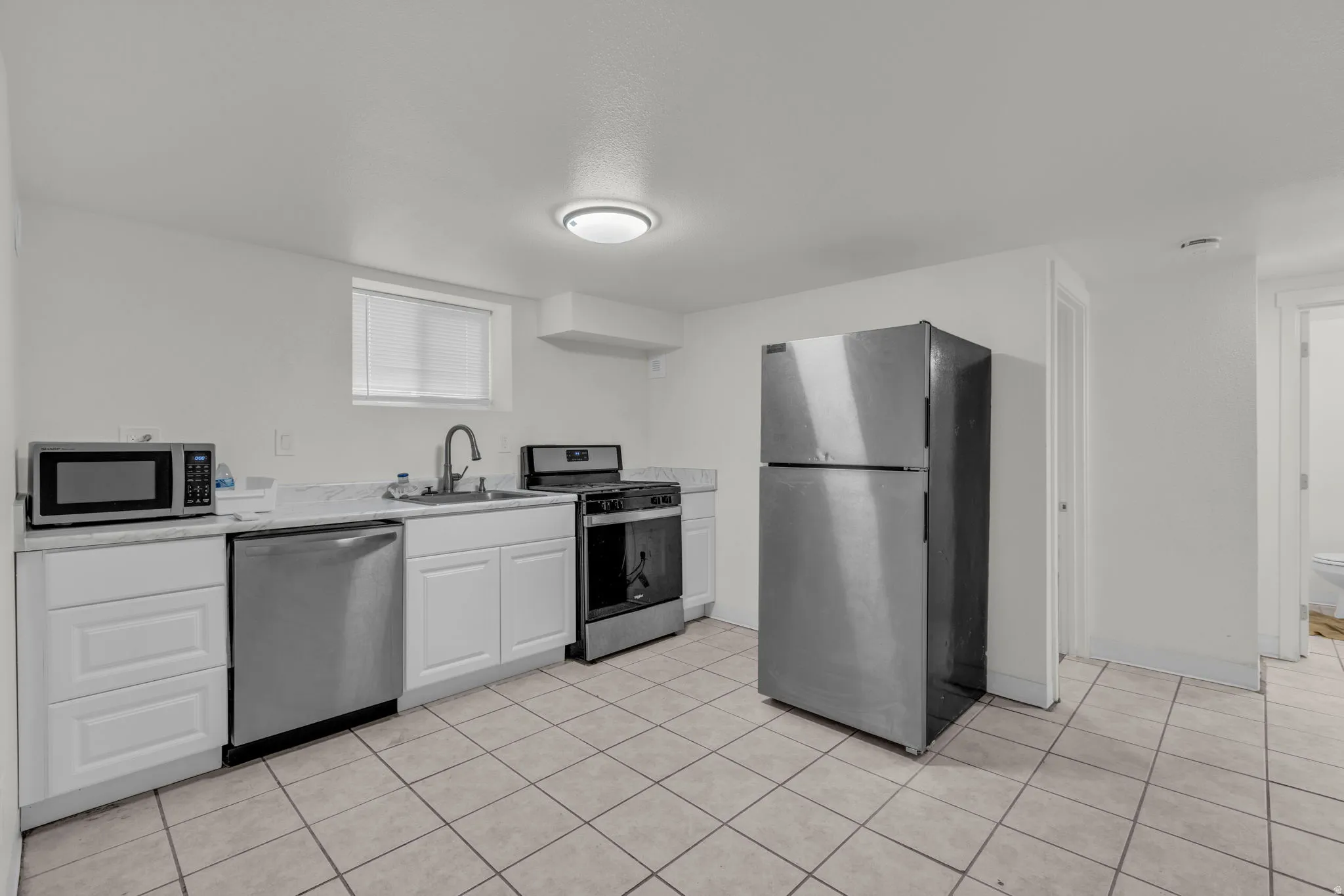 Kitchen featuring stainless steel appliances, light countertops, white cabinets, and light tile patterned floors