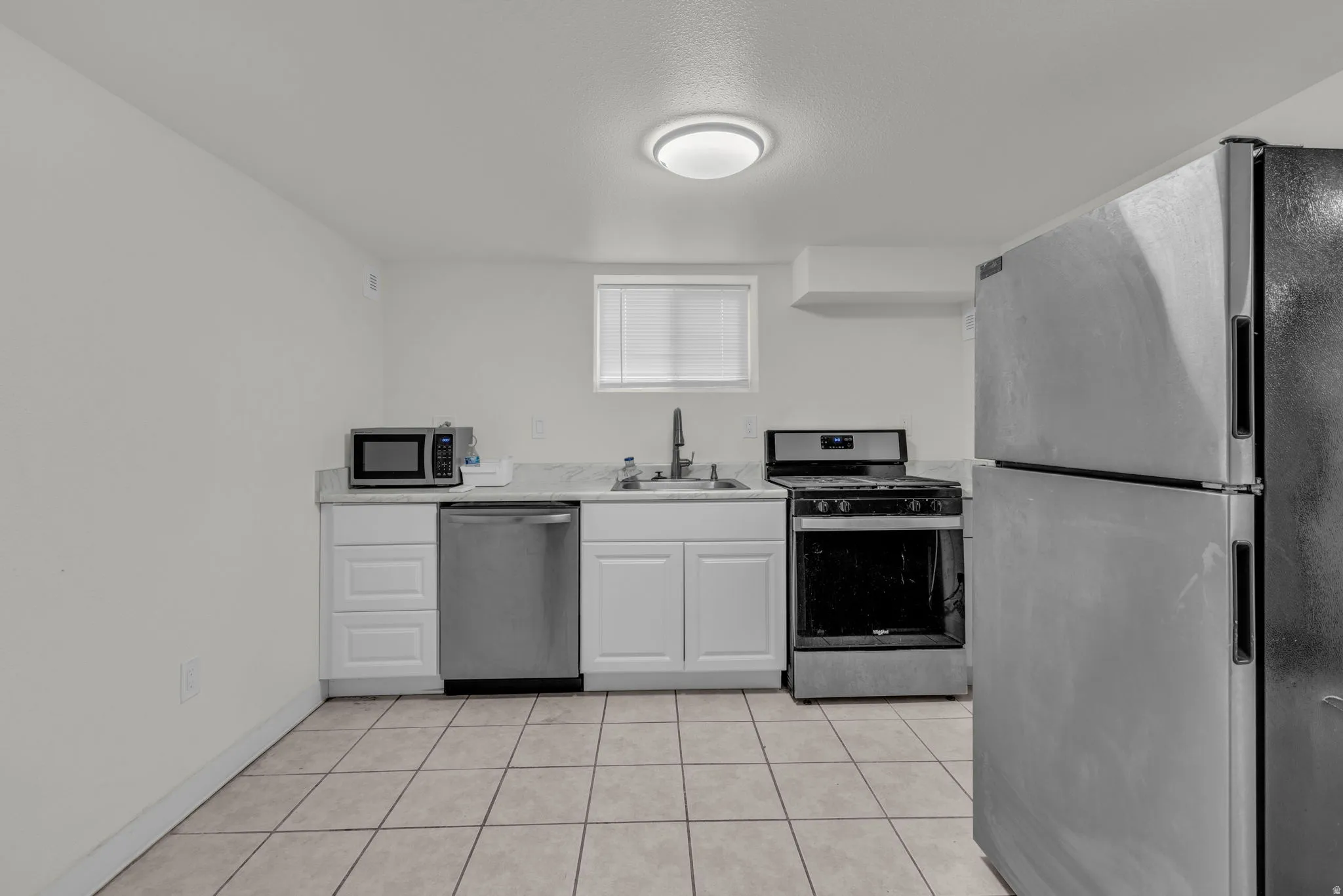 Kitchen with stainless steel appliances, light countertops, white cabinetry, and light tile patterned flooring