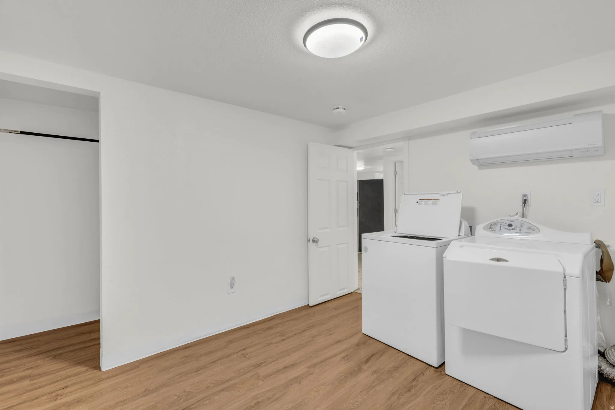 Laundry room with light wood-style flooring, washing machine and dryer, and a mini split for heating / cooling
