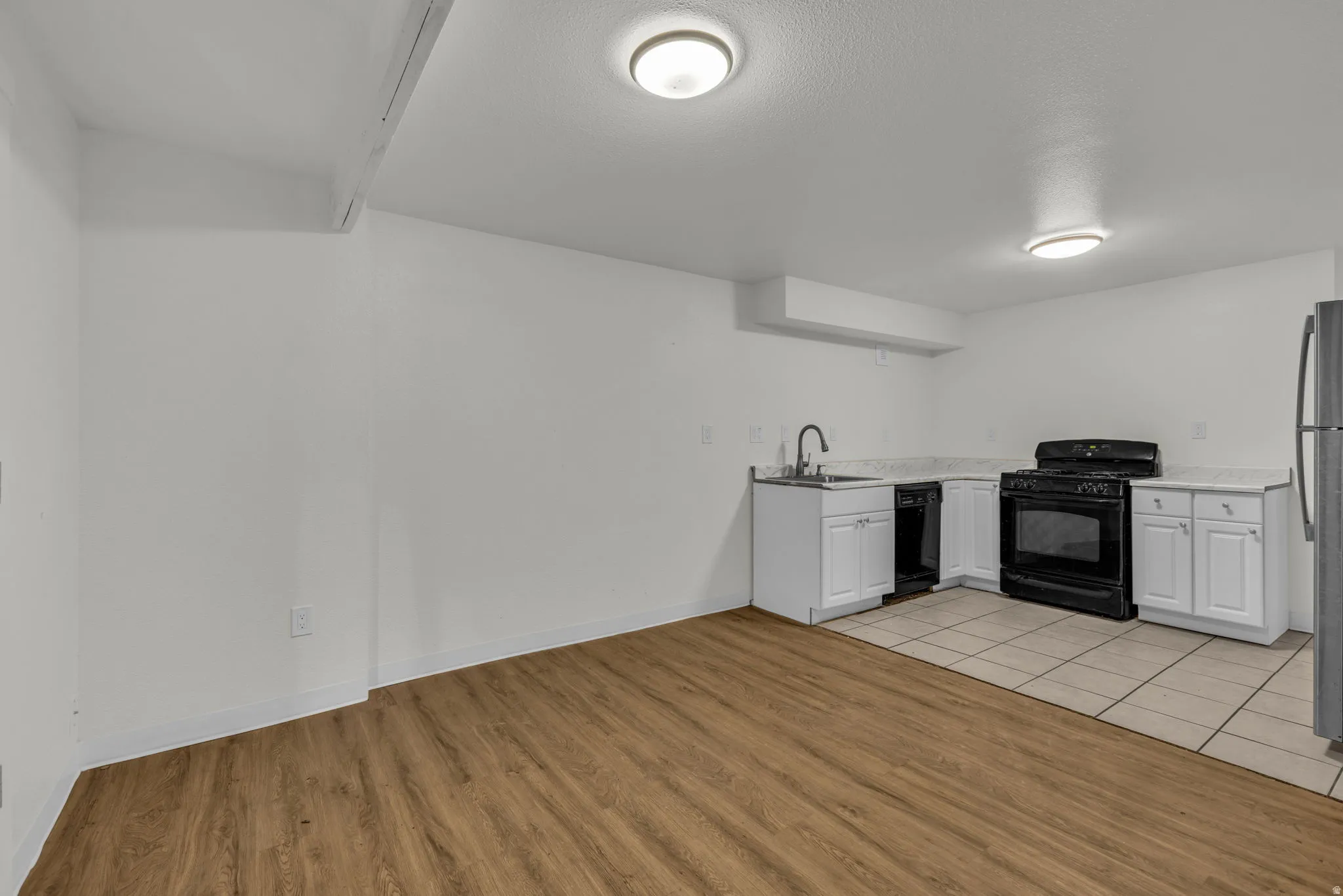 Kitchen with black appliances, white cabinetry, light wood-style flooring, light countertops, and a textured ceiling