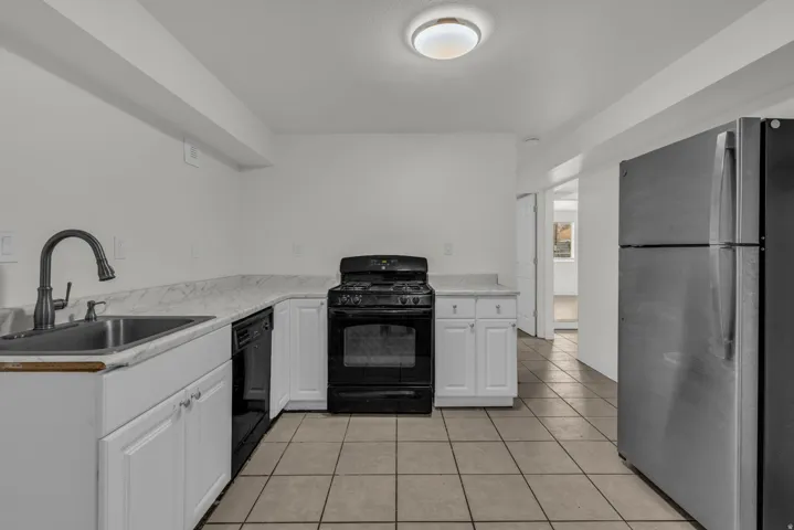 Kitchen with black appliances, light tile patterned floors, light countertops, and white cabinetry