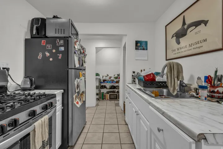 Kitchen featuring stainless steel appliances, light countertops, light tile patterned flooring, and white cabinetry