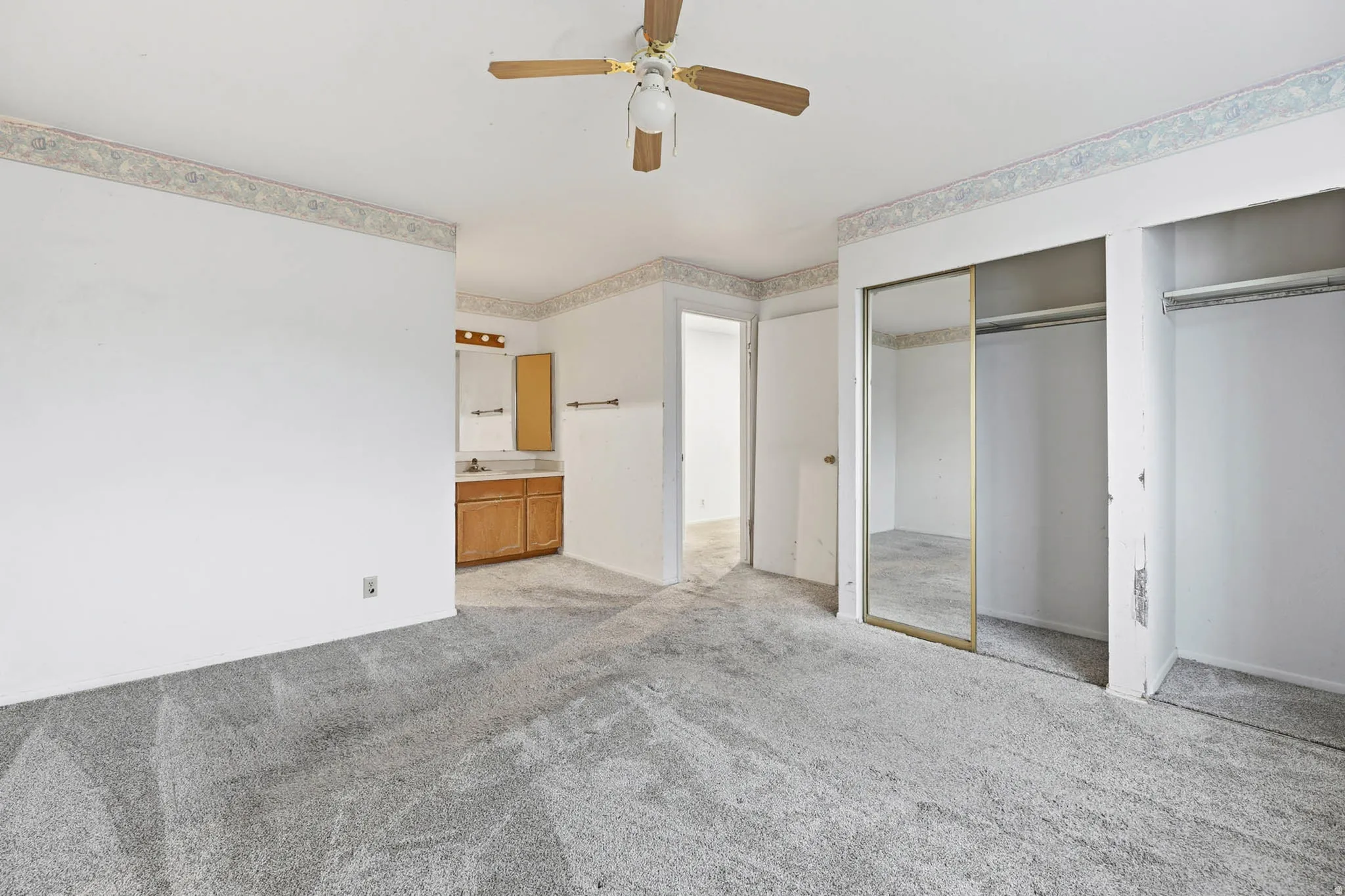 Unfurnished bedroom with light carpet, ensuite bathroom, a ceiling fan, and a closet