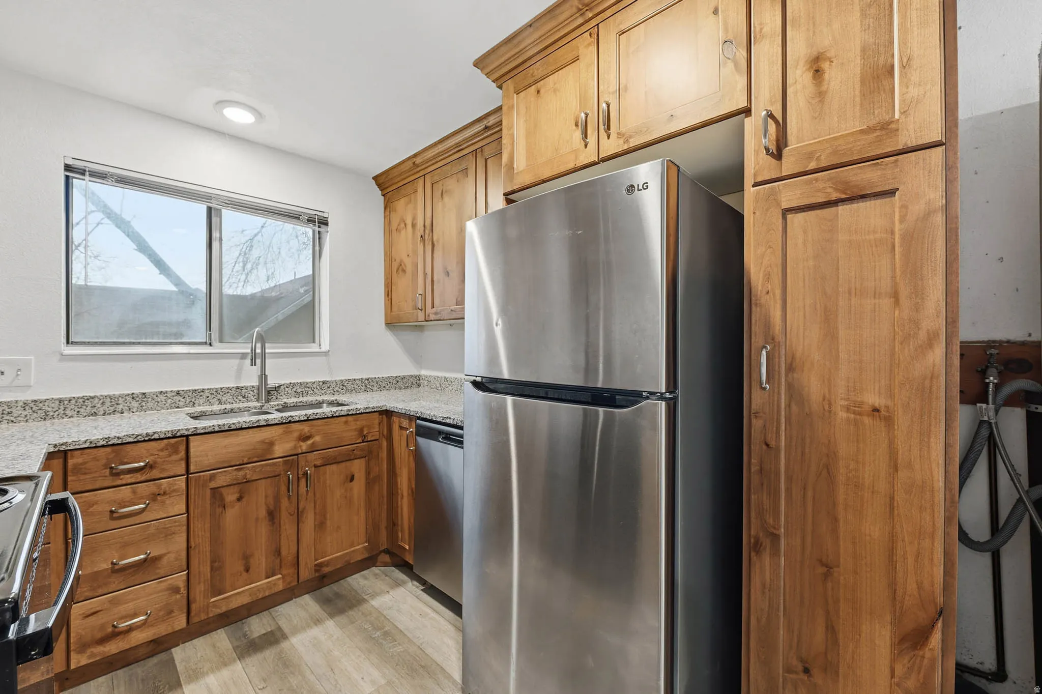 Kitchen featuring stainless steel appliances, light stone counters, wood finish cabinetry, and light wood-style floors