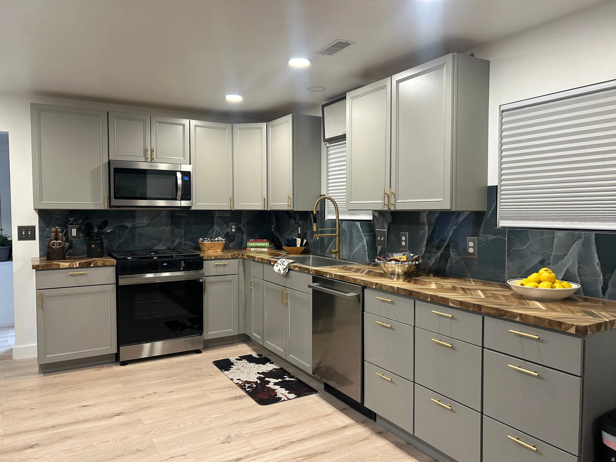 Kitchen featuring gray cabinets, stainless steel appliances, backsplash, light wood-style floors, and recessed lighting
