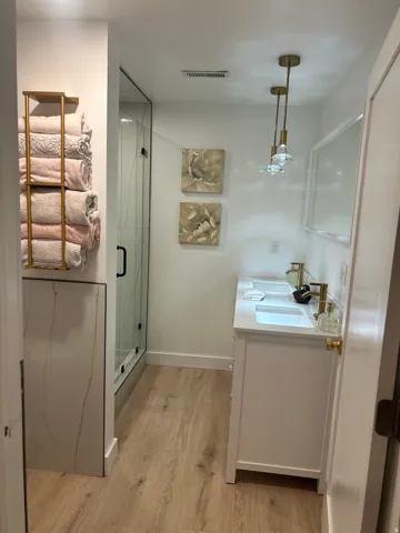Bathroom with vanity, light wood-style floors, and a marble finish shower