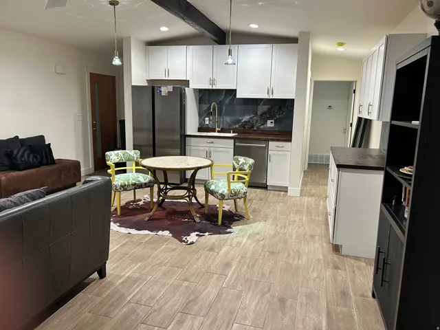 Kitchen with white cabinetry, wood finish floors, stainless steel appliances, vaulted ceiling with beams, and backsplash