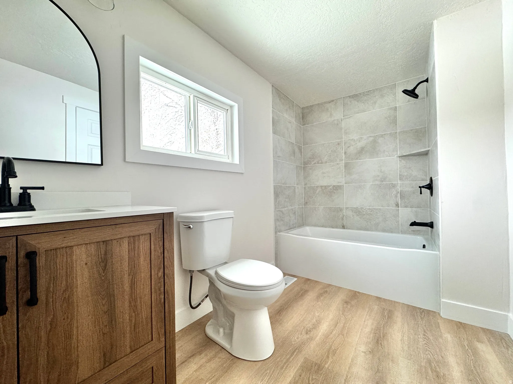 Bathroom featuring vanity, light wood finished floors, shower / bathtub combination, and a textured ceiling