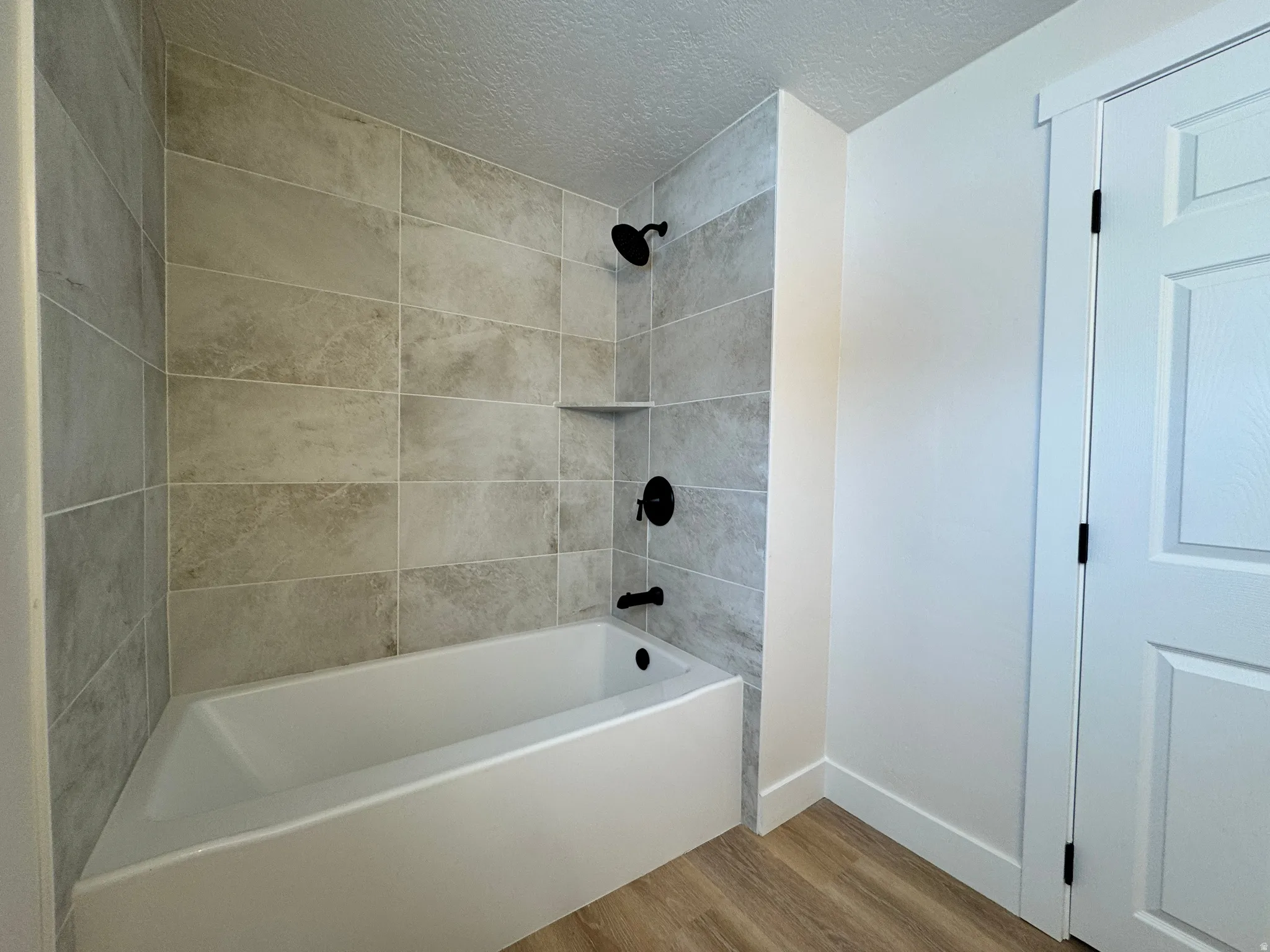 Full bath featuring light wood finished floors, bathing tub / shower combination, and a textured ceiling
