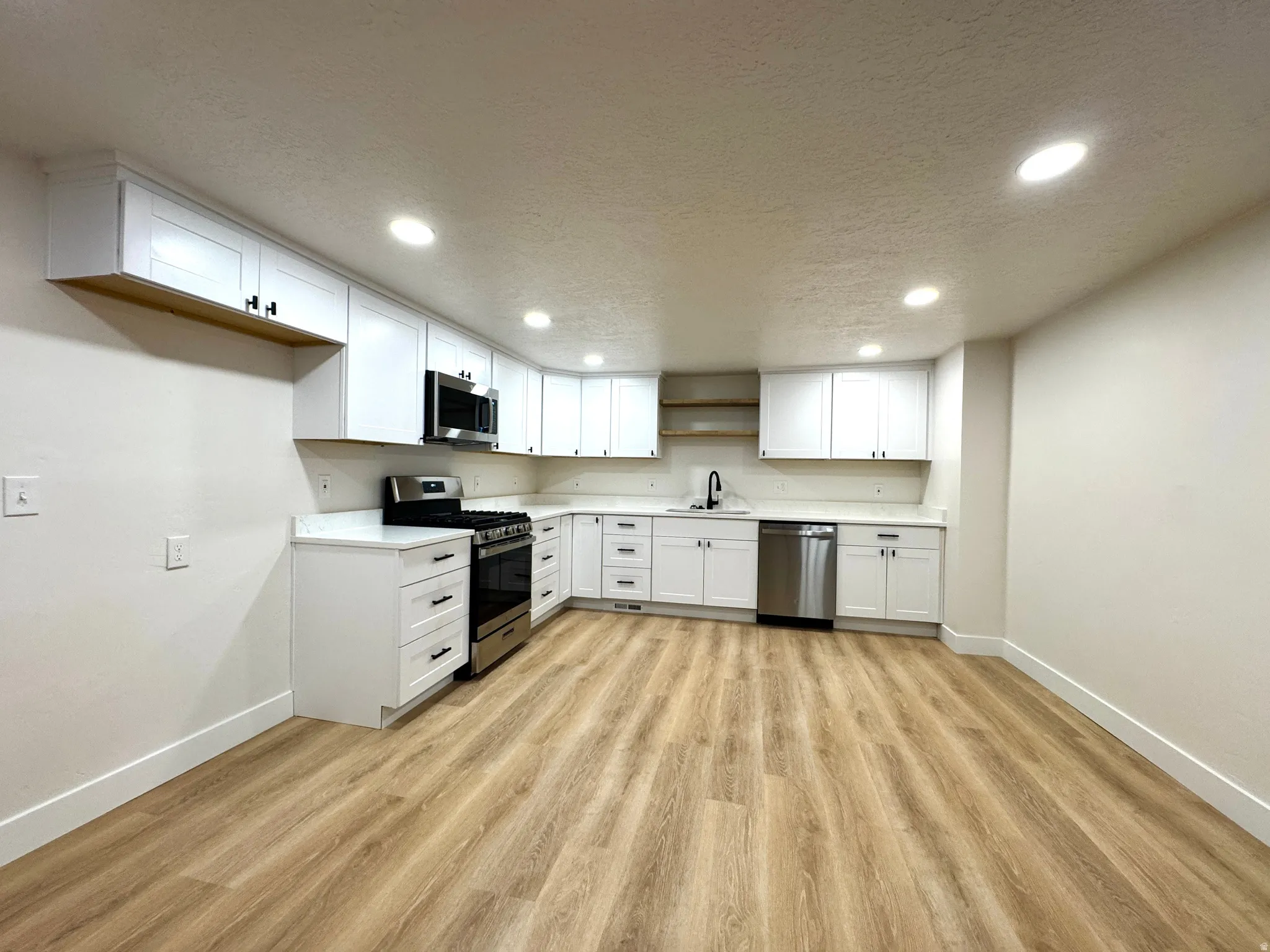 Kitchen with white cabinets, light countertops, stainless steel appliances, light wood-type flooring, and a textured ceiling