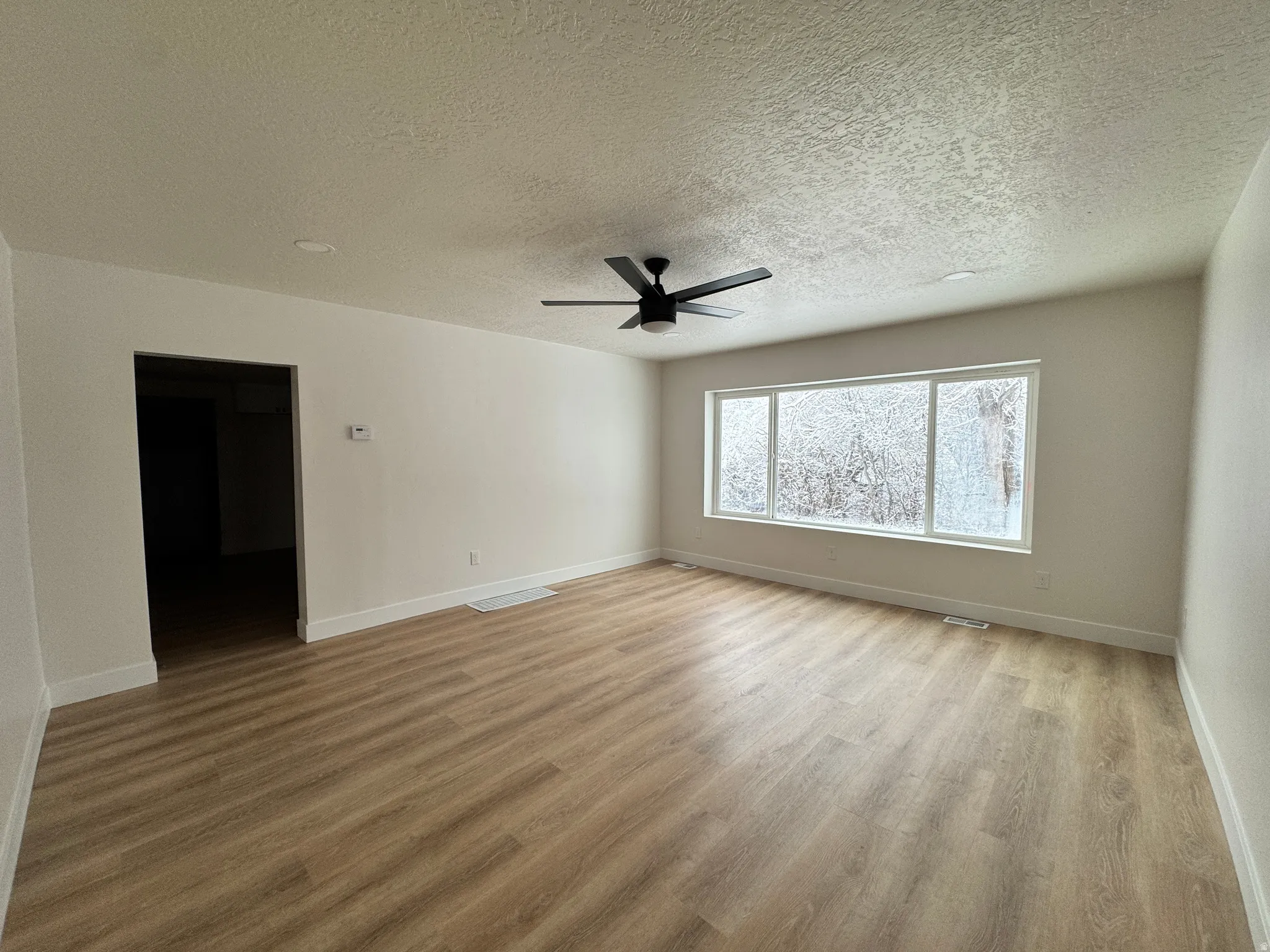 Spare room featuring light wood-type flooring, a textured ceiling, and a ceiling fan