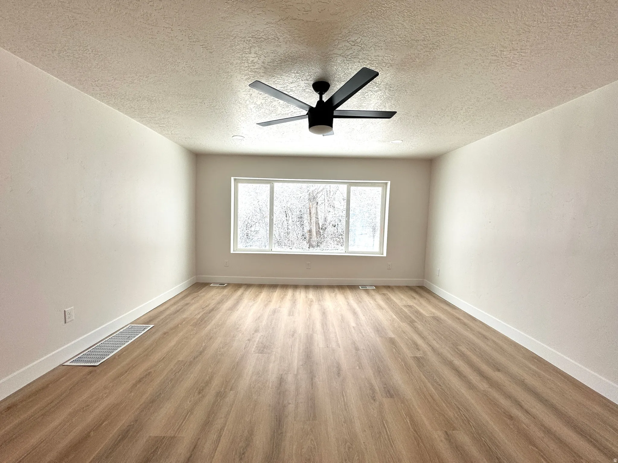 Empty room with light wood finished floors, ceiling fan, and a textured ceiling
