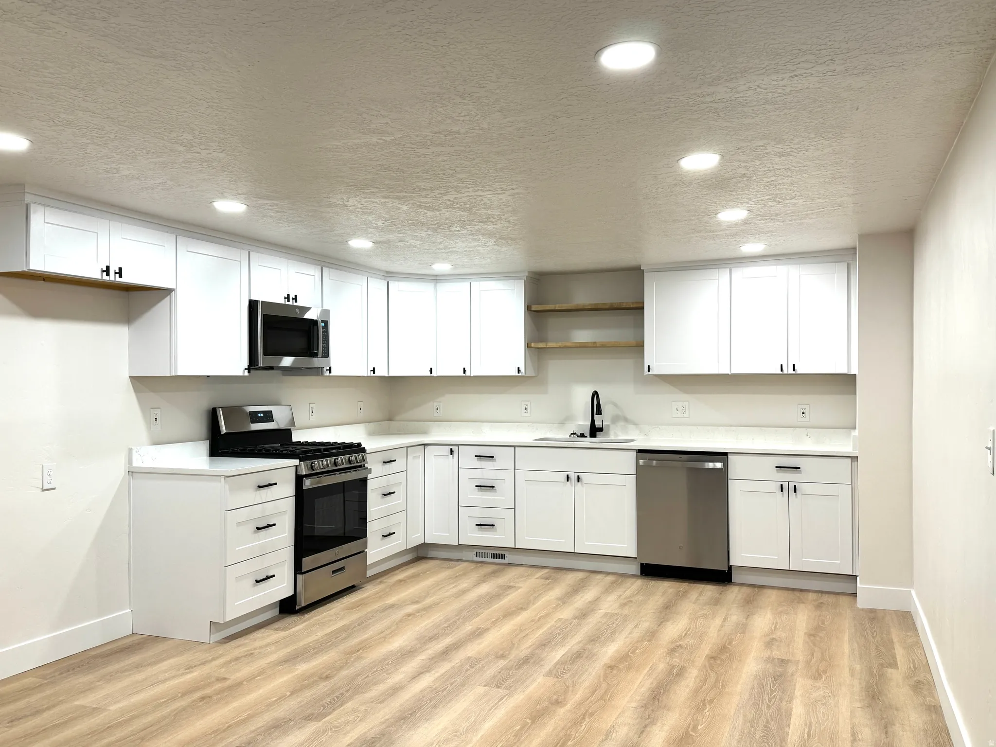Kitchen featuring white cabinetry, a textured ceiling, stainless steel appliances, recessed lighting, and light wood-style flooring