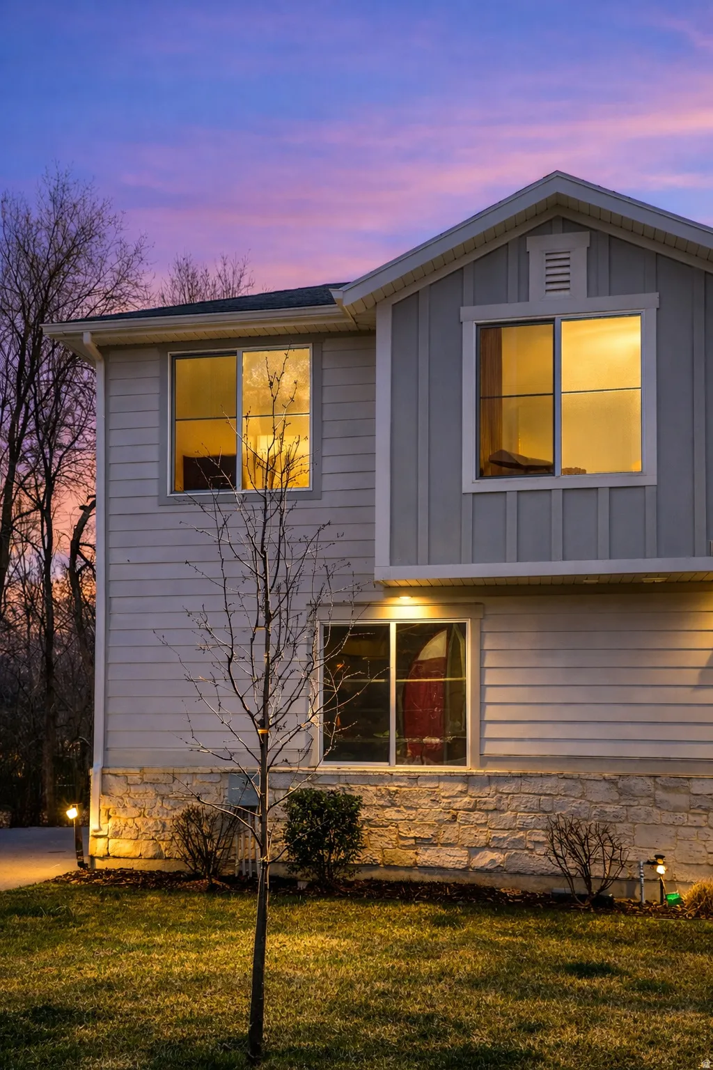 Property exterior at dusk featuring board and batten siding, a yard, and stone siding