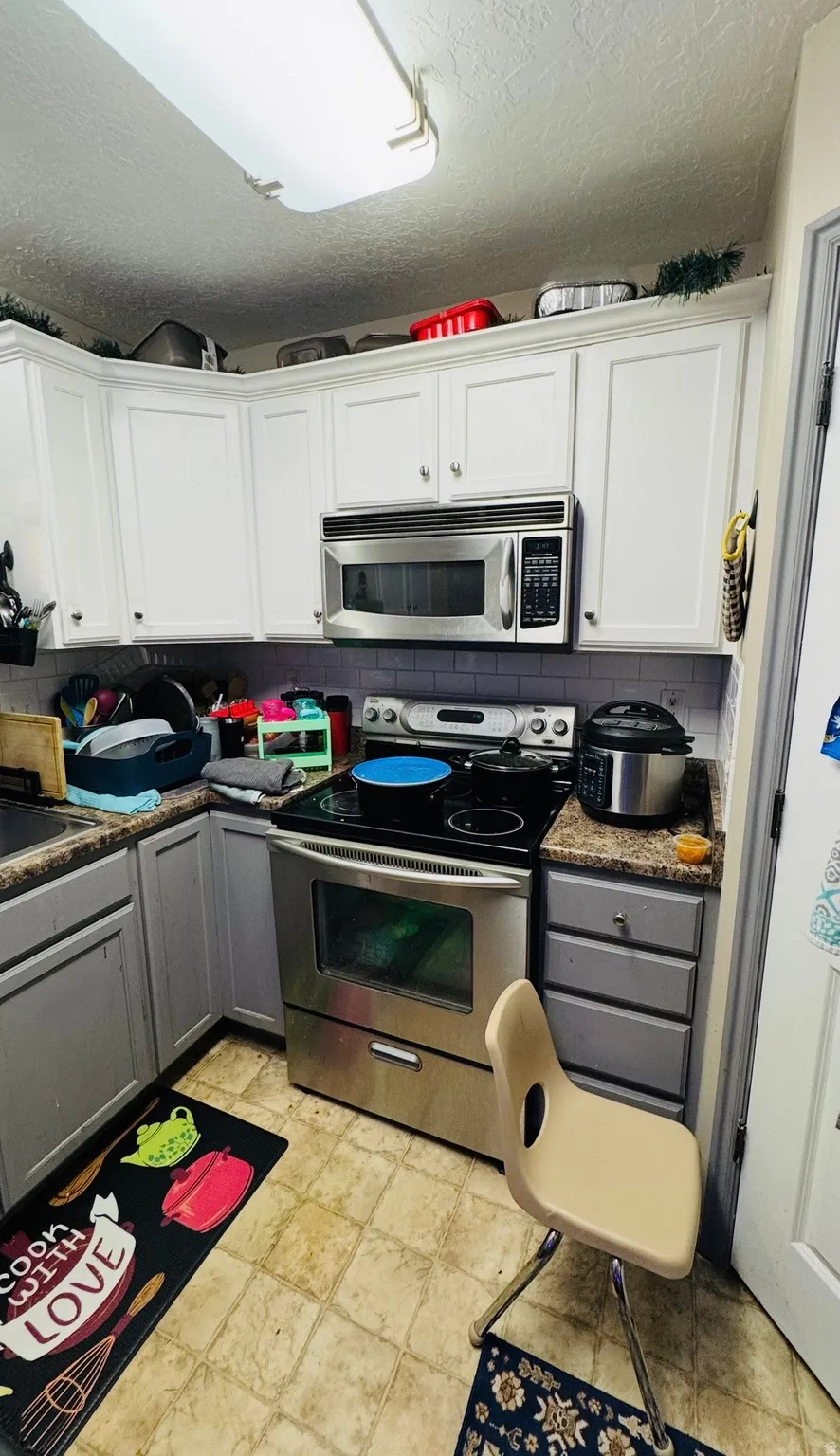 Kitchen with stainless steel appliances, a textured ceiling, two tone cabinetry, and backsplash