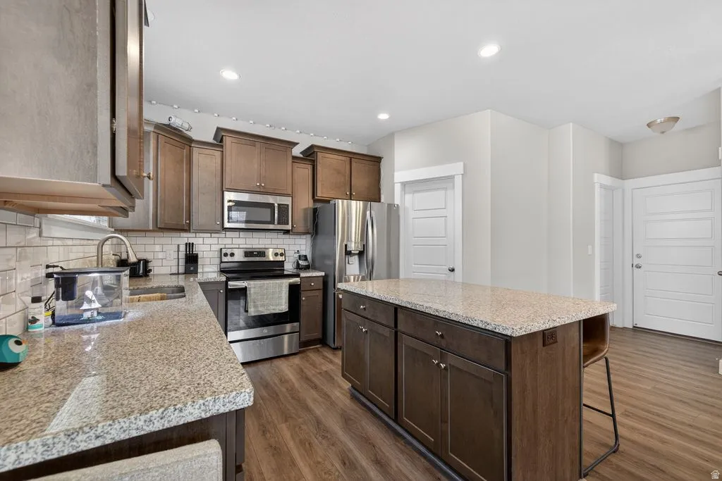 Kitchen with a center island, stainless steel appliances, light stone counters, dark wood-type flooring, and a breakfast bar