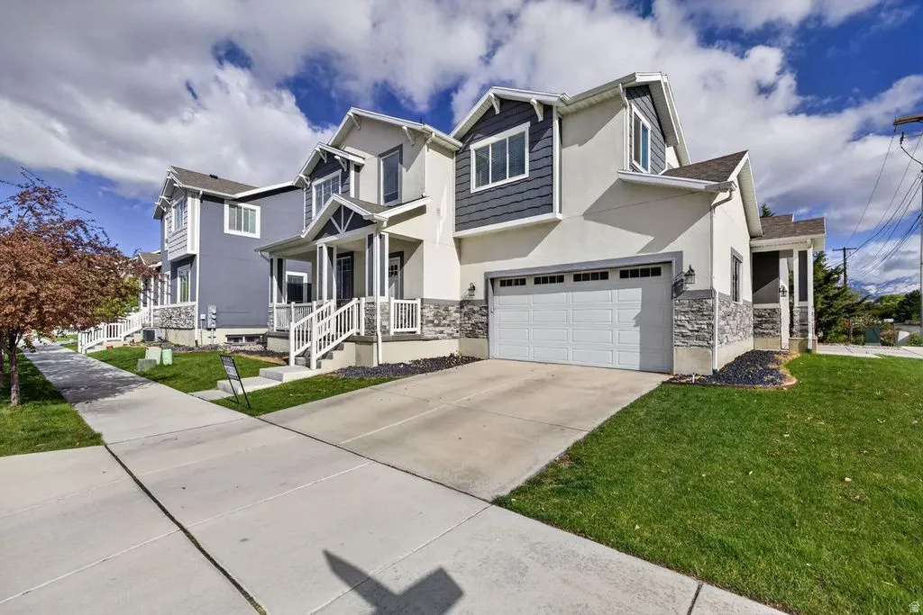 View of front facade with stucco siding, a front lawn, stone siding, and driveway