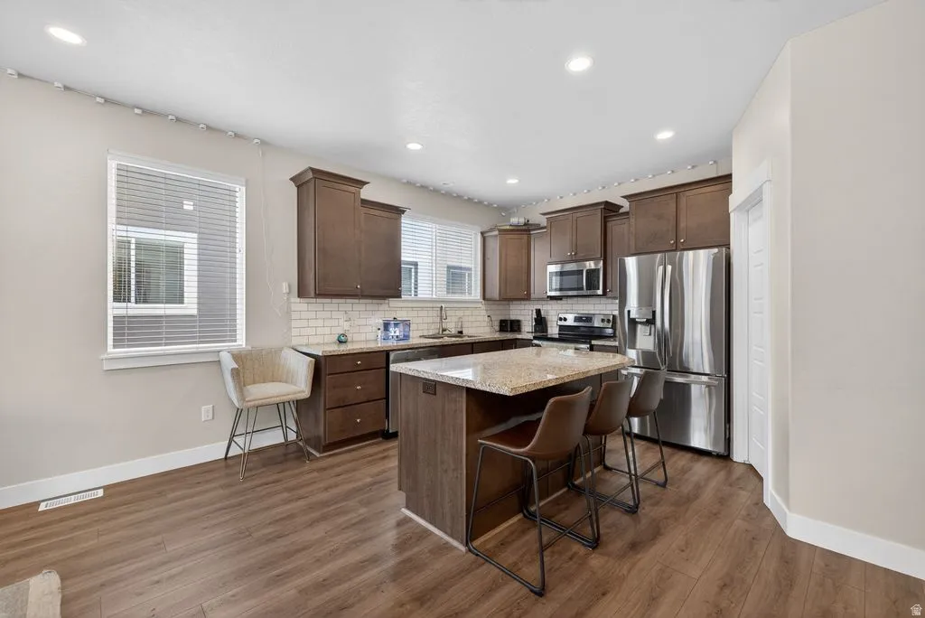 Kitchen with a kitchen island, stainless steel appliances, a breakfast bar area, light stone countertops, and dark wood finish cabinetry