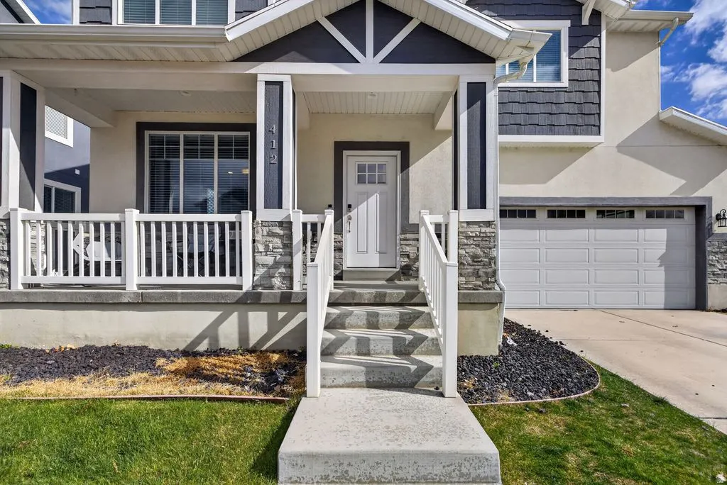View of exterior entry with stucco siding, covered porch, stone siding, and driveway