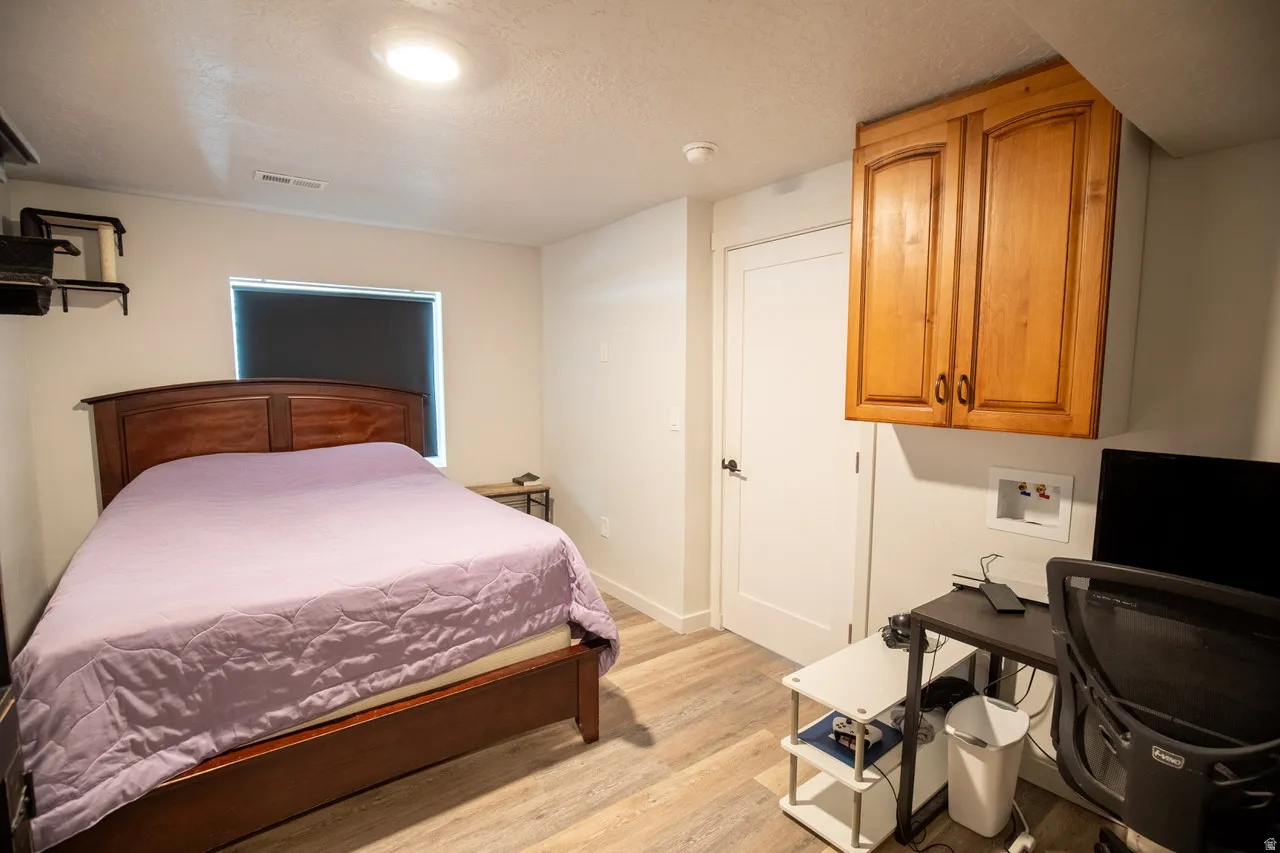 Bedroom with an office area, light wood-style flooring, and a textured ceiling