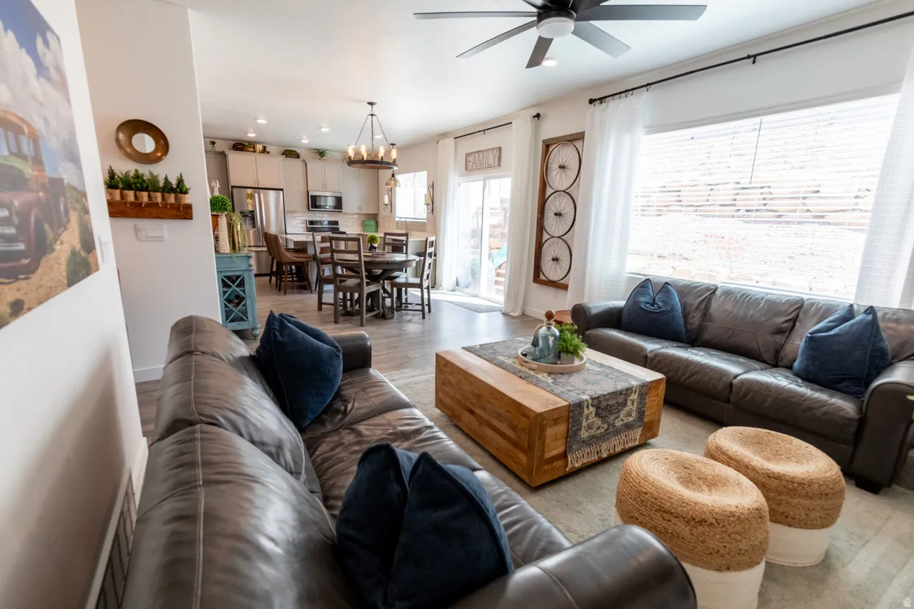 Living room featuring light wood-style flooring, suspended lighting, and a ceiling fan