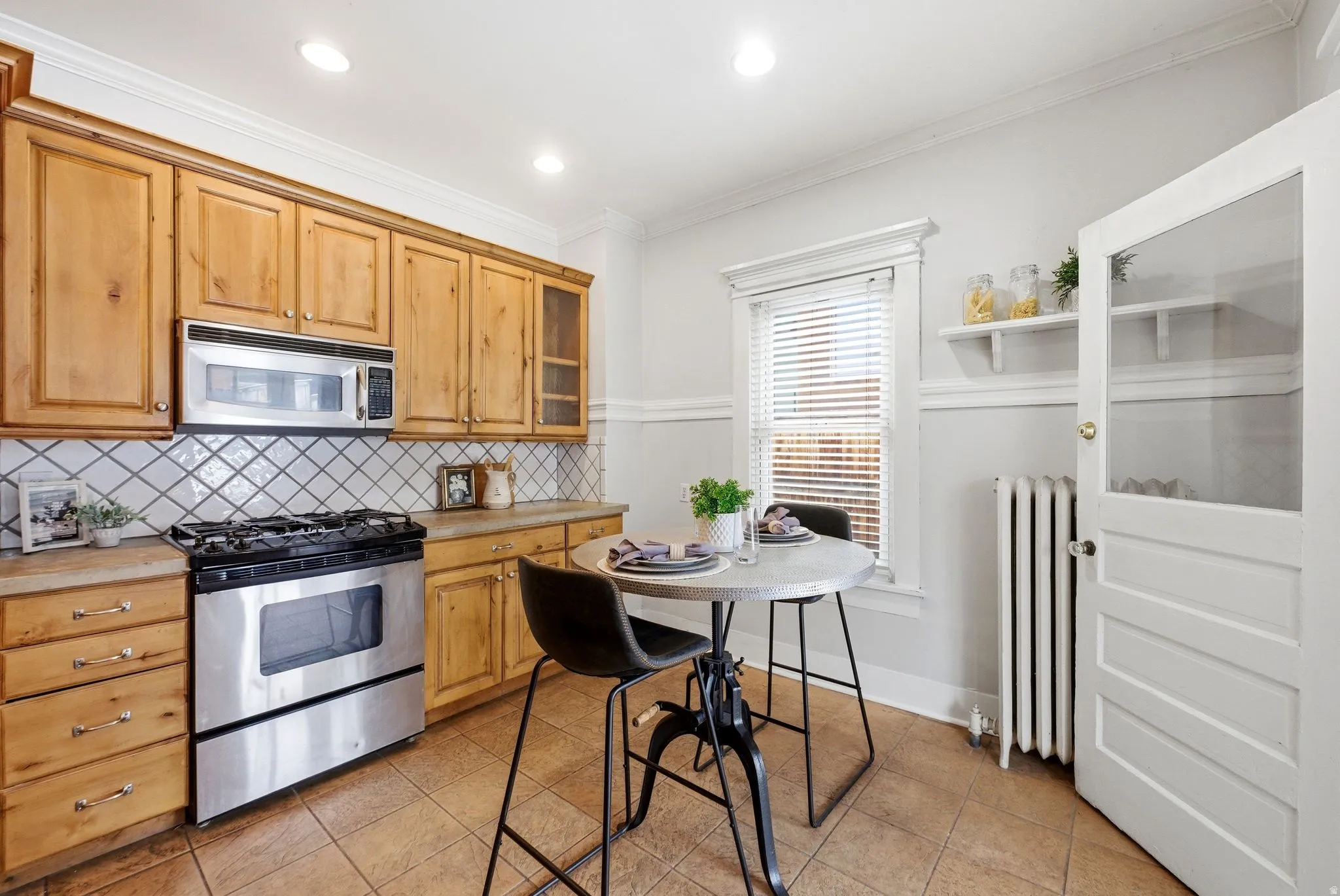 Kitchen with stainless steel appliances, light countertops, radiator heating unit, crown molding, and light tile patterned floors