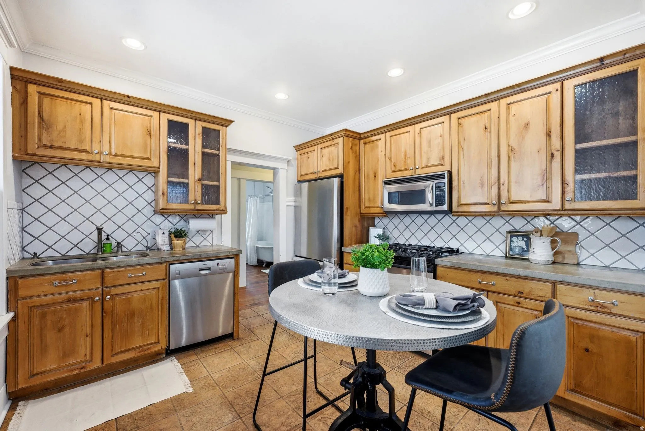 Kitchen with glass fronted cabinets, stainless steel appliances, wood finish cabinets, light tile patterned floors, and ornamental molding