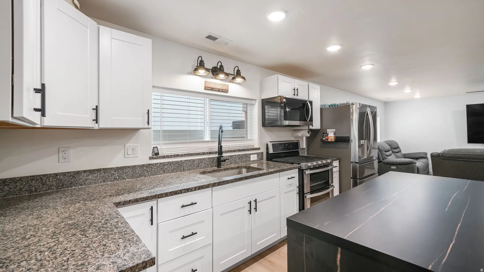 Kitchen with stainless steel appliances, white cabinetry, open floor plan, light wood finished floors, and recessed lighting