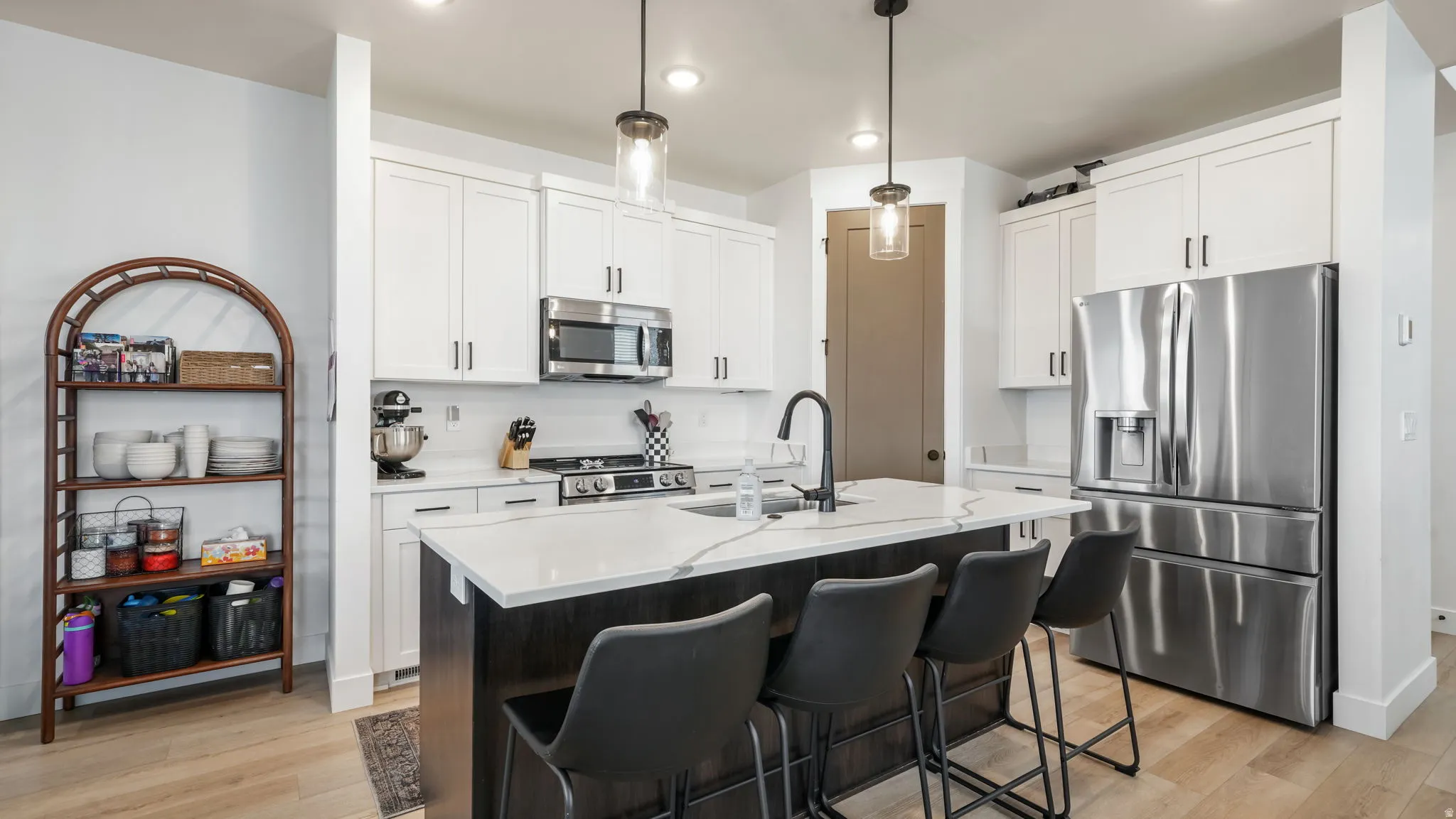 Kitchen featuring stainless steel appliances, an island with sink, white cabinetry, and hanging light fixtures