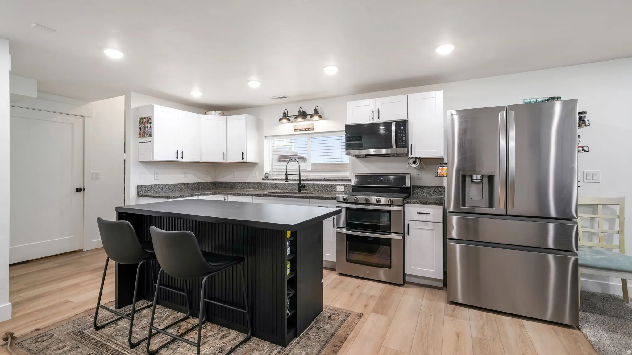 Kitchen with stainless steel appliances, a breakfast bar, a kitchen island, white cabinetry, and light wood-style floors