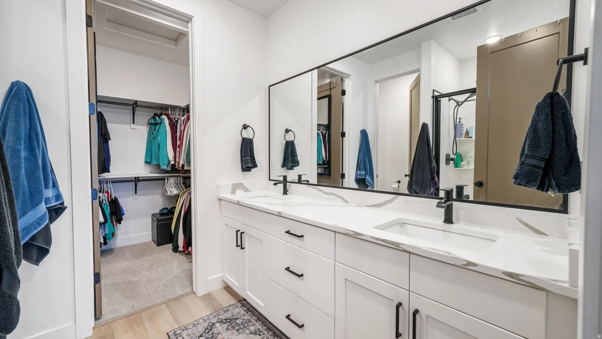 Bathroom featuring double vanity, a spacious closet, light wood finished floors, and a shower stall