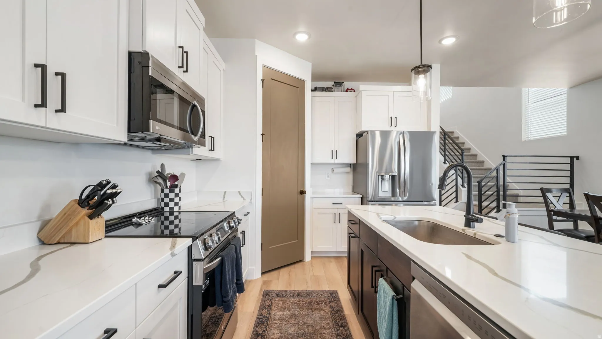 Two tone kitchen featuring stainless steel appliances, light wood-style floors, hanging light fixtures, dual tone cabinetry, and light stone counters