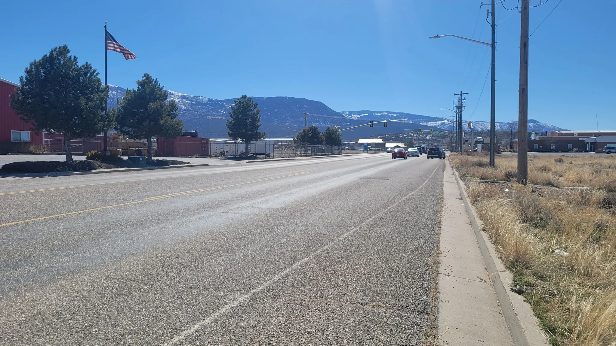 View of asphalt road featuring curbs, street lights, a mountain view, and sidewalks